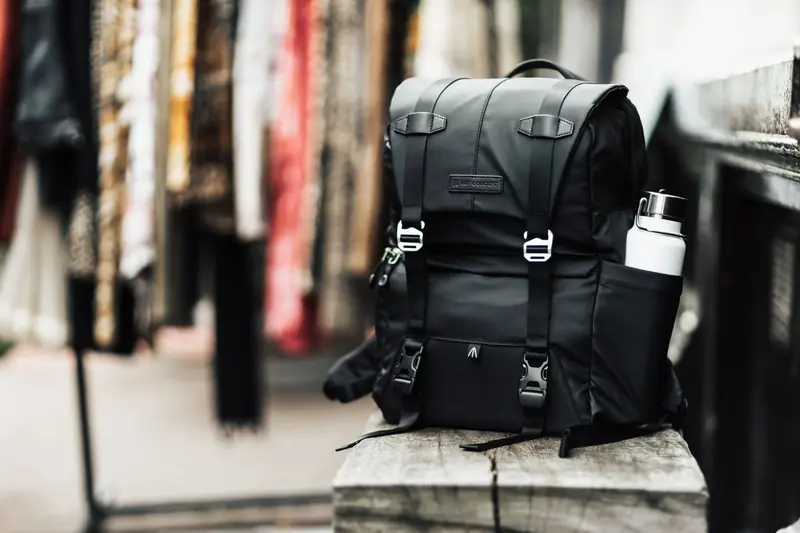 A modern black backpack with a water bottle sits on a wooden bench, ideal for travel enthusiasts